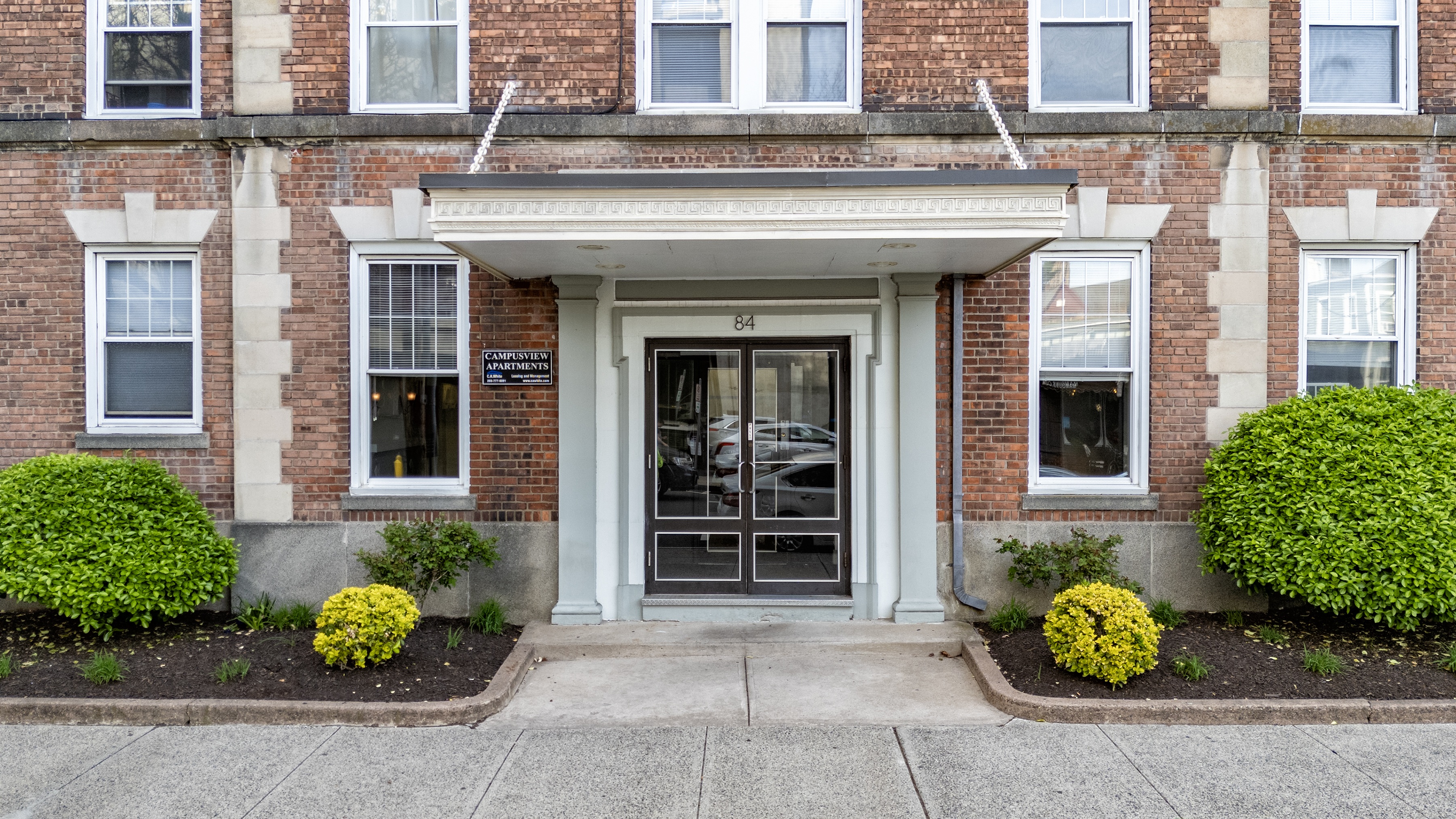 A building with a white door and windows with bushes in front.